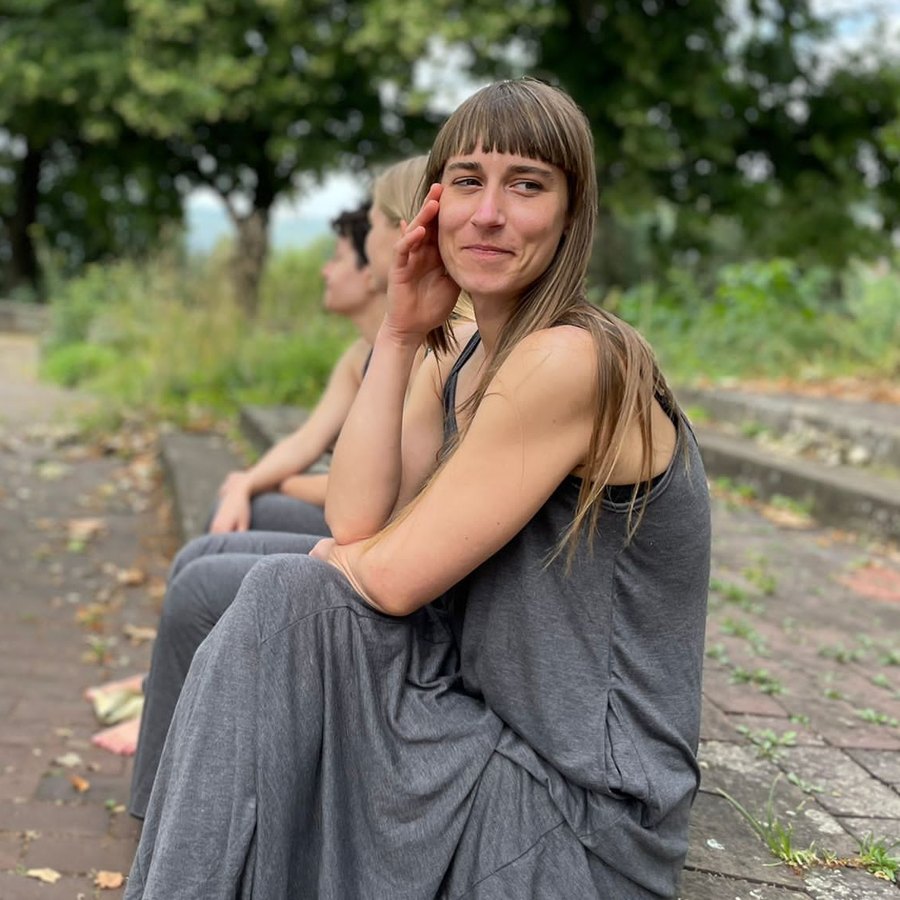 Tina Galinsky sitzt lächelnd auf einer Steinstufe im Park, neben ihr zwei weitere Personen